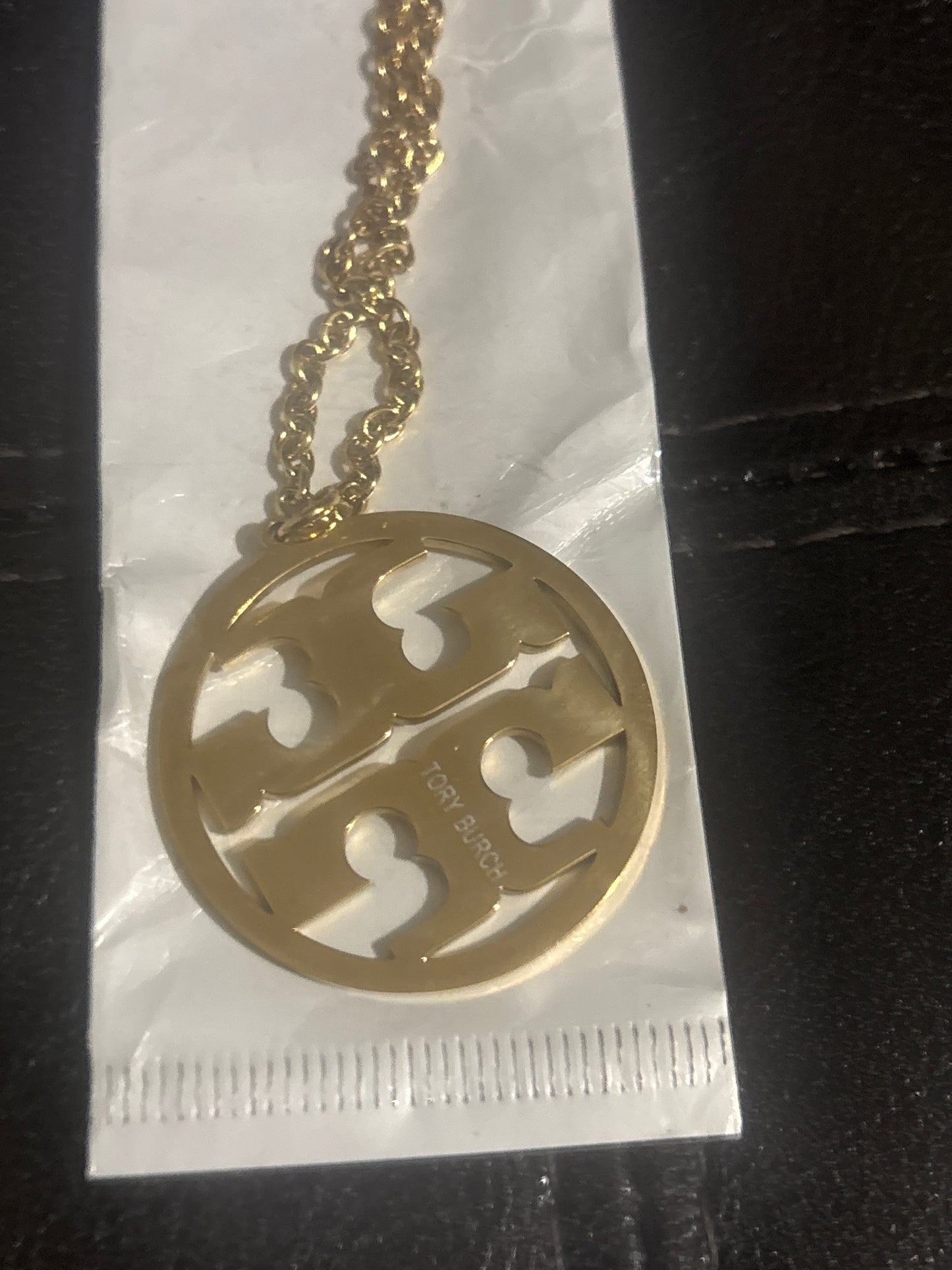 Tory Burch Miller double-T logo circle pendant necklace gold close-up showing TB cut-out detail and TORY BURCH script on pendant